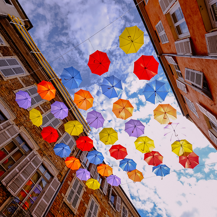 A low angle shot of colorful umbrellas hanging in the middle of buildings with cloudy sky in the background